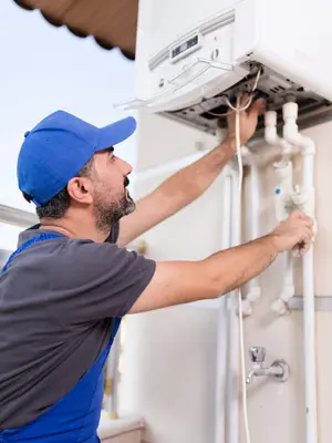 Teknik servis çalışanı kombi cihazı üzerinde bakım veya tamir işlemi yaparken; bağlantı boruları ve kontrol paneli görünmekte