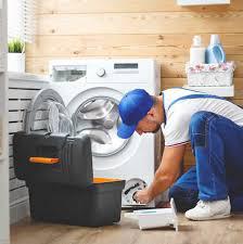 Teknik servis çalışanı çamaşır makinesi tamiri yaparken; servis ortamı ve ekipmanlar görünmekte